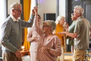 A group of older adults enjoying a dance class together, with one smiling couple in the foreground.
