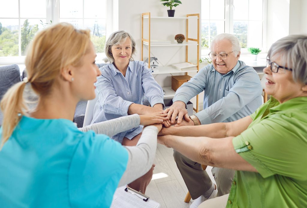 Three seniors working with a nurse, all touching hands and smiling.
